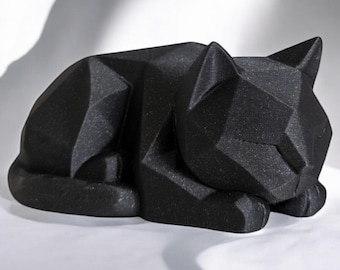 May include: A black geometric cat sculpture in a resting pose. The sculpture is made of a textured material and features a faceted design, with sharp angles and planes creating a modern aesthetic. The cat's ears are upright, and its tail is curled.
