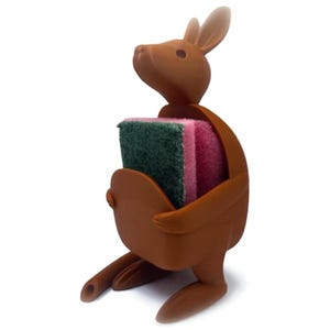 May include: A brown kangaroo-shaped sponge holder with a green and pink sponge. The kangaroo has a pouch to hold the sponge and is designed to sit upright. The ears and head are detailed.