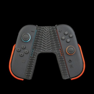 Pode incluir: Controlo de jogos preto e laranja com uma pega central texturizada. O controlo tem botões azuis e laranja, com um fundo preto. O controlo foi concebido para uma consola de jogos.