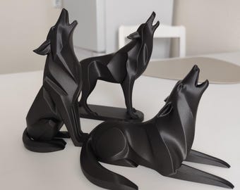 May include: Three black wolf sculptures in various poses, each with its head raised as if howling. One wolf is seated, another standing, and the third is lying down. The sculptures are displayed on a white surface.