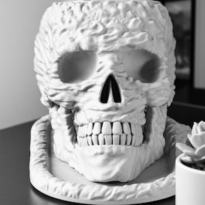 Puede incluir: Un macetero de calavera de cerámica blanca con una superficie texturizada. La calavera tiene una amplia sonrisa con dientes y está sentada sobre una base blanca.