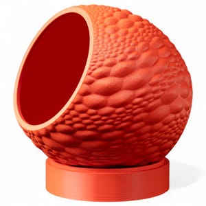 May include: A vibrant orange, spherical pet bed with a textured, scale-like surface. The interior is a deep red, and the bed sits on a matching orange circular base. The opening is large and inviting.