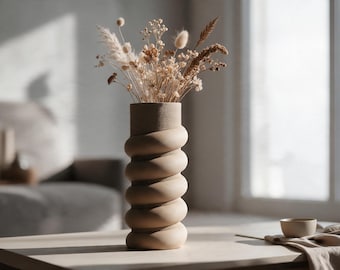 May include: A beige ceramic vase with a spiraled, ribbed cylindrical body holding a bouquet of dried grasses, fluffy pampas, and small white flowers. The vase has a matte, textured finish and a straight, smooth opening at the top.