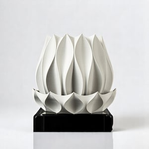 Könnte beinhalten: Eine weiße, abstrakte Skulptur, die einer Lotusblume ähnelt, mit geschichteten, blütenblattartigen Formen. Die Skulptur steht auf einem schwarzen, rechteckigen Sockel, was einen auffälligen Kontrast erzeugt. Modernes und minimalistisches Design.