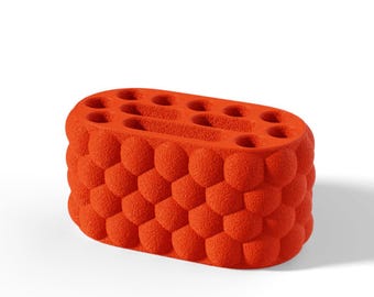 May include: An oval-shaped orange desk organizer with a textured, bubble-like exterior surface. The top features multiple circular and elongated slots designed for holding pens, pencils, or other small office supplies in an upright position.