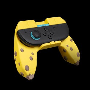 Könnte beinhalten: Ein gelb-brauner Videospiel-Controller in Bananenform. Der Controller hat eine schwarze Mitte mit Knöpfen und einen blauen Joystick. Das Bananen-Design umfasst braune Flecken und eine braune Spitze.