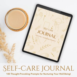 May include: A digital tablet displaying a self-care journal with a beige background and gold illustrations of hands, leaves, and a planet. The text "SELF-CARE JOURNAL WITH DAILY JOURNALING PROMPTS" is displayed on the tablet. The tablet is on a white surface with a cup of coffee and a dried flower arrangement.