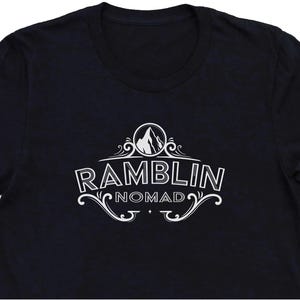 Puede incluir: Camiseta negra con un dise&ntilde;o gr&aacute;fico blanco de un pico de monta&ntilde;a y el texto "Ramblin Nomad".