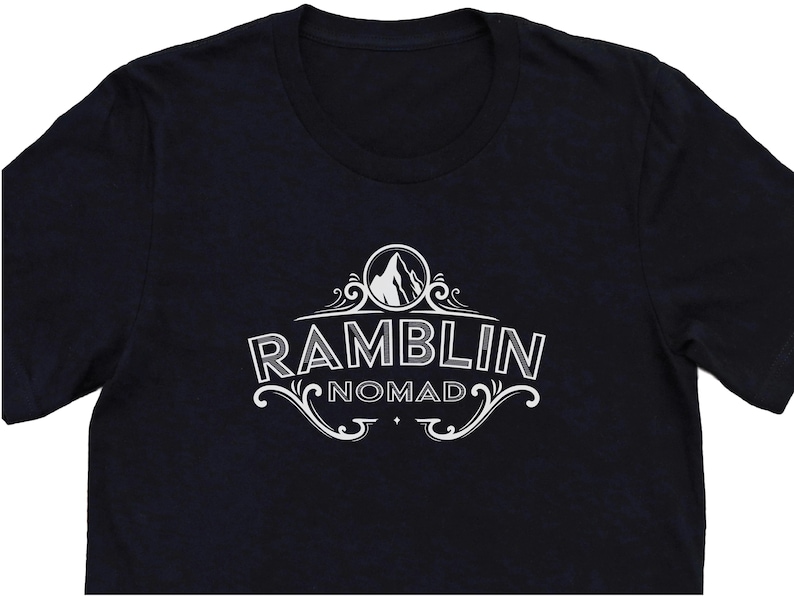 Puede incluir: Camiseta negra con un dise&ntilde;o gr&aacute;fico blanco de un pico de monta&ntilde;a y el texto "Ramblin Nomad".