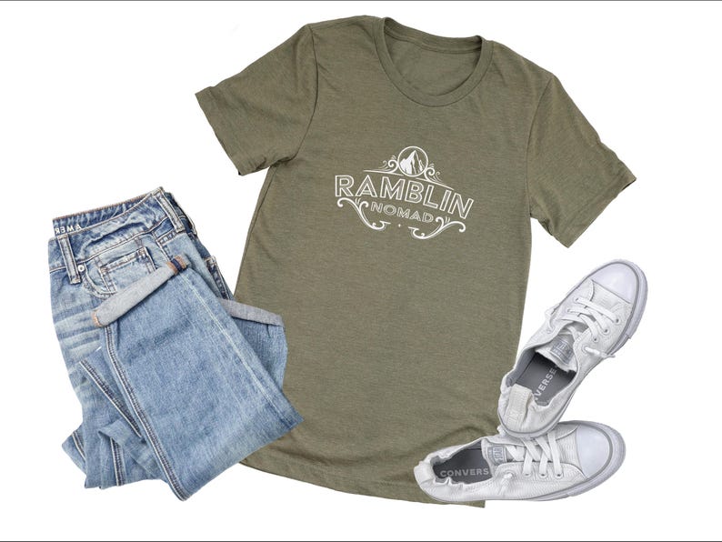 Puede incluir: Una camiseta verde con el texto "Ramblin Nomad" en letras blancas. La camiseta se combina con unos vaqueros azules y unas zapatillas blancas.