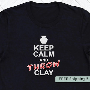 May include: Black t-shirt with the text "KEEP CALM AND THROW CLAY" in white and red. A white vase graphic is above the text. The shirt is a crew neck style.