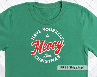 May include: Green t-shirt with the phrase "Have Yourself a Merry Little Christmas" in a circular design. The word "Merry" is in red script, and the other words are in white.