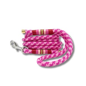 May include: A pink and white braided dog lead with a silver metal clasp. The lead has red and gold accents near the handle and the clasp. The lead is coiled on a white background.