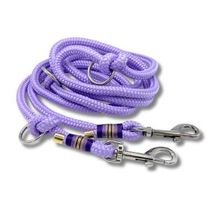Könnte beinhalten: Eine lavendelfarbene Hundeleine mit passendem Halsbandring und zwei silberfarbenen Metallverschlüssen. Die Leine hat dekorative Bänder in Lila, Gold und Marineblau. Das Seil ist eng gewebt und aufgerollt.