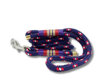 May include: A navy blue dog leash with red and white accents woven into the rope. The leash has purple and gold bands and a silver metal clasp. The rope is coiled and ready for use.