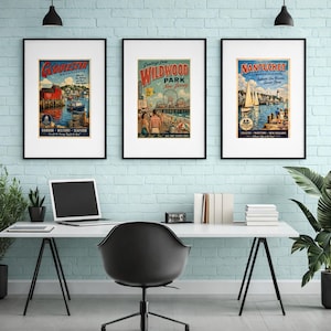 May include: Three framed vintage travel posters. The posters feature colorful illustrations of Gloucester, Massachusetts; Wildwood Park, New Jersey; and Nantucket, Massachusetts. The posters are displayed above a white desk with a laptop and office supplies.
