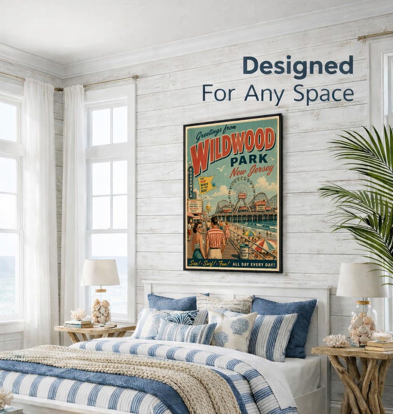 May include: A framed vintage-style poster with the text "Greetings from Wildwood Park New Jersey" hangs above a bed with blue and white striped bedding. The poster features a boardwalk scene with a Ferris wheel. The room has white walls and a coastal theme.