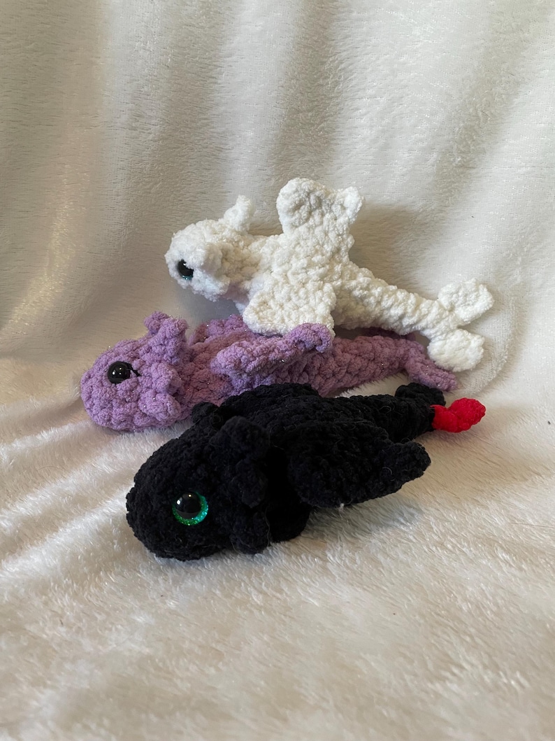 May include: Three crocheted dragon plushies. One is white, one is purple, and one is black with green eyes.
