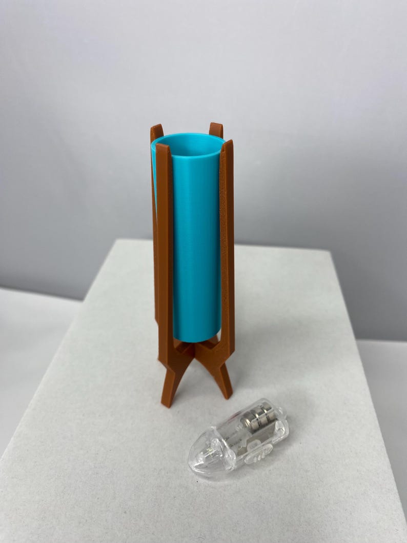 May include: A teal cylinder lamp with a brown wooden stand. The lamp has a clear plastic light bulb next to it. The lamp is a mid-century modern design.