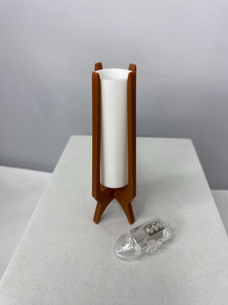 May include: A mid-century modern style lamp with a brown wooden frame and a white cylindrical shade. The lamp has a tripod base. A small, clear plastic object is next to the lamp.