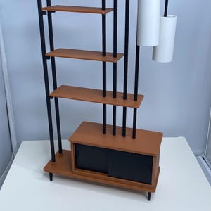 May include: A mid-century modern style bookshelf with a brown finish, black vertical supports, and a cabinet with sliding doors. Two white cylindrical lamps hang from the top.