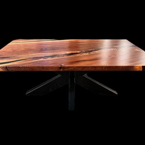 May include: A wooden coffee table with a black epoxy resin inlay and a black X-shaped base.