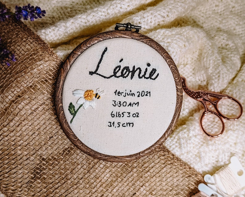 Embroidery with name and birth details of a baby (date of birth, time of birth, weight and height) with a flower and a bee as a decoration