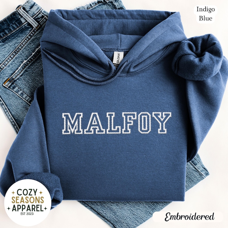 Peut inclure: Un sweat &agrave; capuche bleu indigo avec le mot "MALFOY" brod&eacute; en blanc. Le sweat &agrave; capuche a une capuche &agrave; cordon et est fait d'une mati&egrave;re douce. L'image montre &eacute;galement un jean bleu.