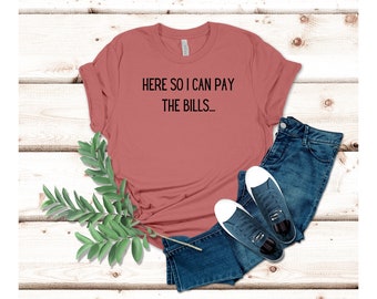May include: A maroon t-shirt with the text "HERE SO I CAN PAY THE BILLS_" printed in black.