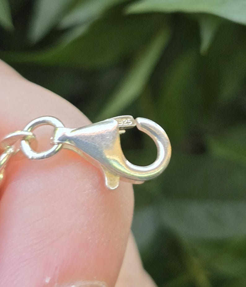 May include: A silver-toned lobster claw clasp attached to a chain link. The metal surface of the clasp features a small, clearly engraved 925 hallmark, indicating sterling silver composition. The clasp mechanism is shown in an open position.