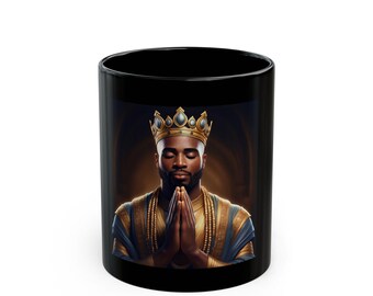 Puede incluir: Taza de cerámica negra con una imagen de un hombre con corona dorada y vestiduras azules y doradas. El hombre tiene las manos juntas en oración, sobre un fondo cálido y dorado. Un artículo decorativo.
