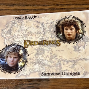 May include: A rectangular card featuring characters from "The Lord of the Rings." The card has a map background with portraits of Frodo Baggins and Samwise Gamgee. The title "The Lord of the Rings" is prominently displayed.