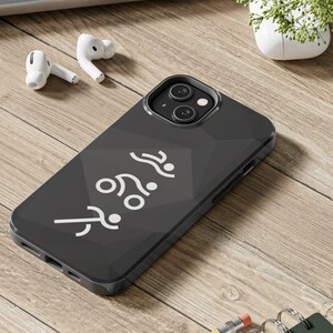 May include: A black phone case with a white graphic of three swimmers. The case is on a wooden surface with a pencil and a notebook.