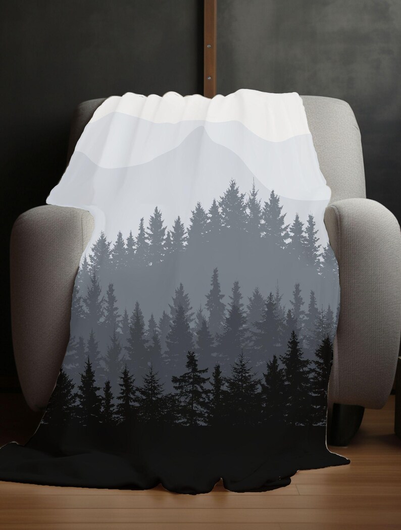 May include: A soft, white throw blanket with a black and grey silhouette of a forest and mountains. The blanket is draped over a grey armchair.