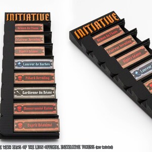 May include: A black plastic initiative tracker stand with orange lettering at the top. It features eight horizontal slots holding rectangular game tokens with French text including Demon du Chaos, Eclaireur Vermling, Vipere Geante, and others.