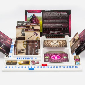 Pode incluir: Um organizador de jogos de tabuleiro em pl&aacute;stico branco com ranhuras para cartas, fichas e uma pista numerada de 0 a 22. O tabuleiro exibe componentes de jogo, incluindo cartas rotuladas como Geminate, Cloak of Pockets, Heavy Basinet e Battle Axe.
