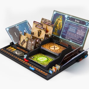 Pode incluir: Um organizador de jogos de tabuleiro em pl&aacute;stico preto com uma trilha numerada de 0 a 22, ranhuras para v&aacute;rias cartas de jogo e um grande painel de personagem com a etiqueta Brute. O organizador cont&eacute;m v&aacute;rias cartas ilustradas, fichas e marcadores.