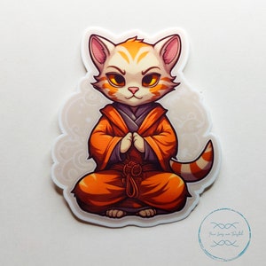 Puede incluir: Un gato blanco y naranja con una túnica naranja, un cinturón negro y un nudo rojo. El gato está sentado en una postura meditativa con las patas cruzadas delante de él. El gato tiene una expresión seria en su rostro.
