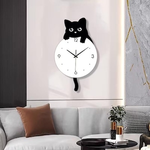 May include: A black cat-shaped wall clock with a white clock face. The cat is perched above the clock, with its tail hanging below. The clock has black hands and simple dot hour markers. A decorative piece for a living room or bedroom.