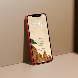 Op de afbeelding: Een rode iPhone met een digitale klok die 11:47 uur aangeeft en de datum zondag 23 juli. De achtergrond is een beige landschap met een citaat in zwarte tekst: "Zoek niet naar plezier omwille van het plezier zelf." - Miyamoto Musashi.