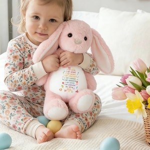 May include: A soft pink bunny toy with long ears, featuring embroidered text: "I AM KIND, I AM SMART, I AM BRAVE, I AM CONFIDENT, I AM CAPABLE, I AM GRATEFUL, I AM LOVED, I AM ENOUGH." The bunny is held by a child.