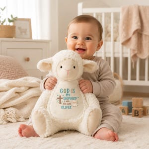 May include: A plush white lamb stuffed animal with embroidered text that reads God is my shepherd I am his lamb Oliver, featuring a brown cross, small green leaves, and a tiny lamb illustration on the center of its soft, textured belly.
