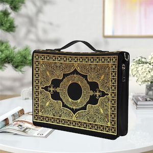 May include: A black and gold decorative bag with a handle and a shoulder strap. The bag has an ornate gold design on a black background, with a central circular motif. The bag is rectangular and appears to be made of a durable material.