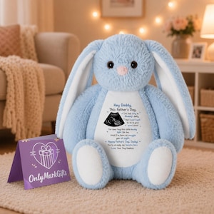 May include: A light blue plush bunny with long ears and a pink nose. The bunny has a message printed on its belly that reads "Hey Daddy, This Father's Day." A purple card with the text "Only Mark Gifts" is in front of the bunny.