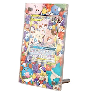 Może przedstawiać: Przezroczysta akrylowa ramka ekspozycyjna zawierająca japońską kartę kolekcjonerską Pokémon Tag Team GX. Ramka posiada kolorowy nadruk na obrzeżach przedstawiający różne postacie Pokémon, Poké Balle oraz owoce, mocowana czterema srebrnymi śrubami.