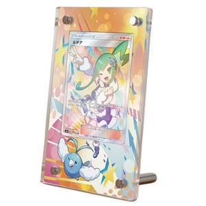 May include: A clear acrylic display frame holding a Japanese Pokémon trading card featuring the character Lisia and the Pokémon Altaria. The frame has four silver metal corner screws and a colorful background print with stars and geometric shapes.