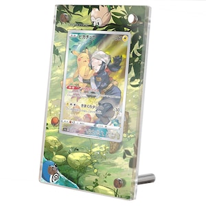 May include: A clear acrylic display case with a Japanese Pokemon card featuring Pikachu and a character. The card has a green, blue, and white background with the text "ピカチュウ" and "60". The display case has a green, blue, and white background with a small, brown, and white owl.