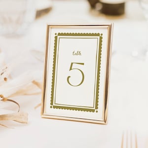 May include: Gold framed table number card with a scalloped border. The card says "table 5" in a gold font.