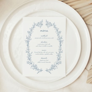 Może przedstawiać: Niebieska i biała karta menu z kwiatową ramką. Menu zawiera koktajl, przystawkę, danie główne i deser. Tekst brzmi: "menu, koktajl: moskiewska muła z granatu i żurawiny, przystawka: sałatka z mieszanych zielonych z kozim serem i winegretą szalotkową, danie główne: duszone wołowe wargi z sosem z czerwonego wina, pieczone ziemniaki, mieszane warzywa, deser: glazurowana tarta z gruszką, słony karmelowy sernik"