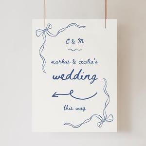 May include: A white sign with blue lettering and a blue ribbon design. The sign reads "C & M, markus & cecilia's wedding, this way".